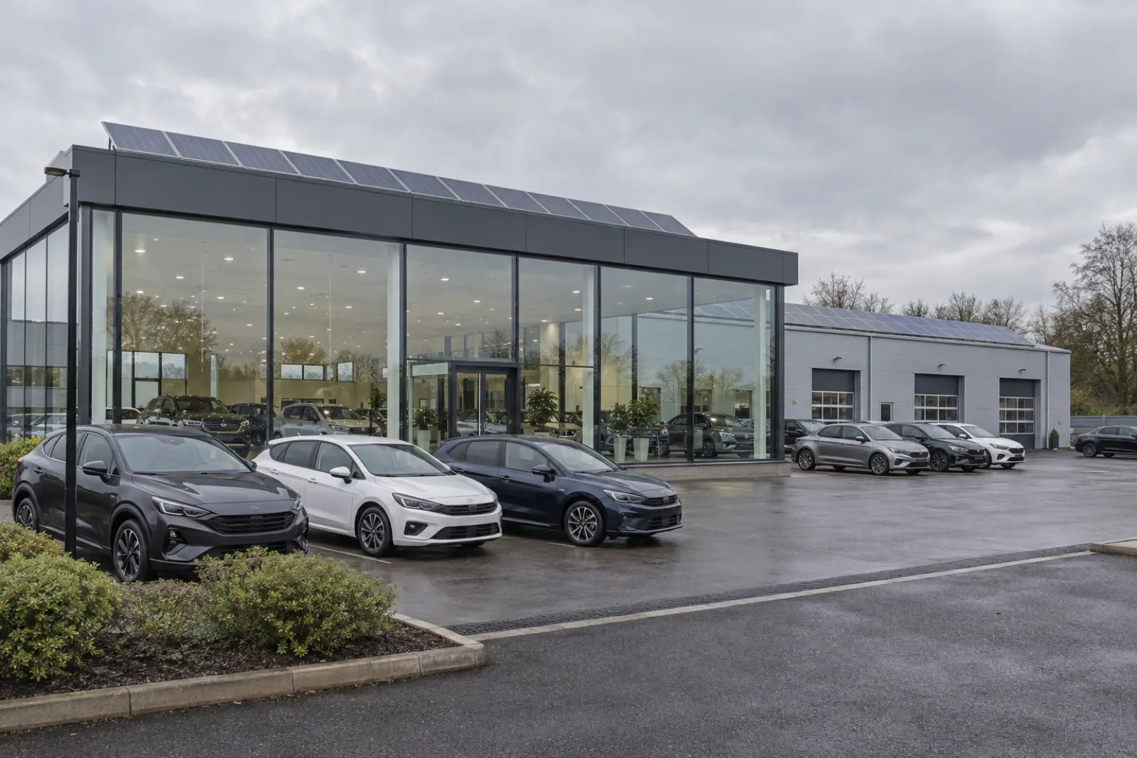 A car dealership showroom and workshop, both roofs carrying solar panels, with cars on the forecourt