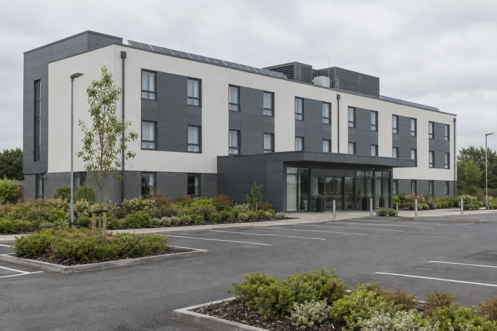 A three storey roadside hotel with a solar array on its flat roof beside the rooftop plant