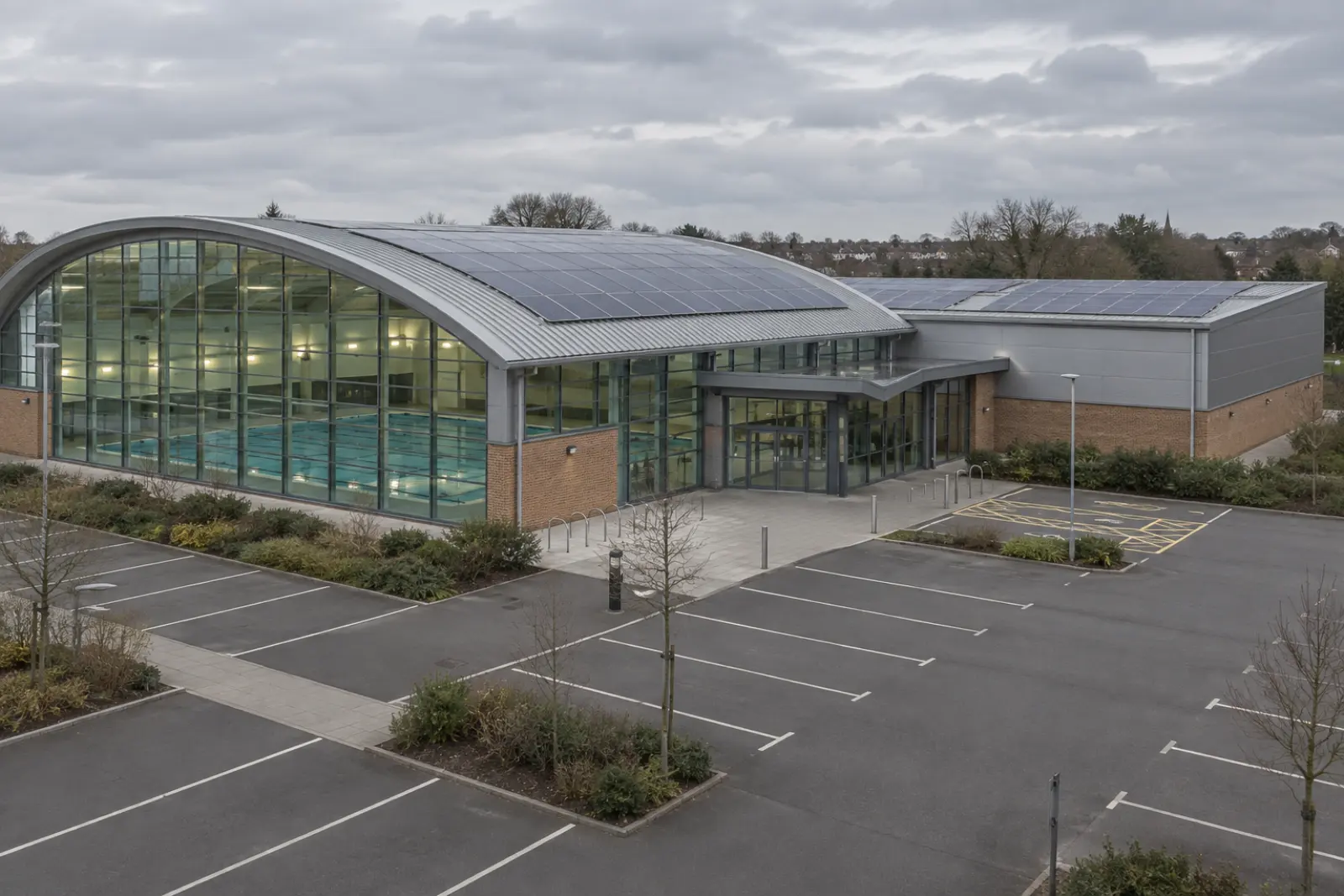 A leisure centre with solar panels across the pool hall roof and the lower sports hall block beside it