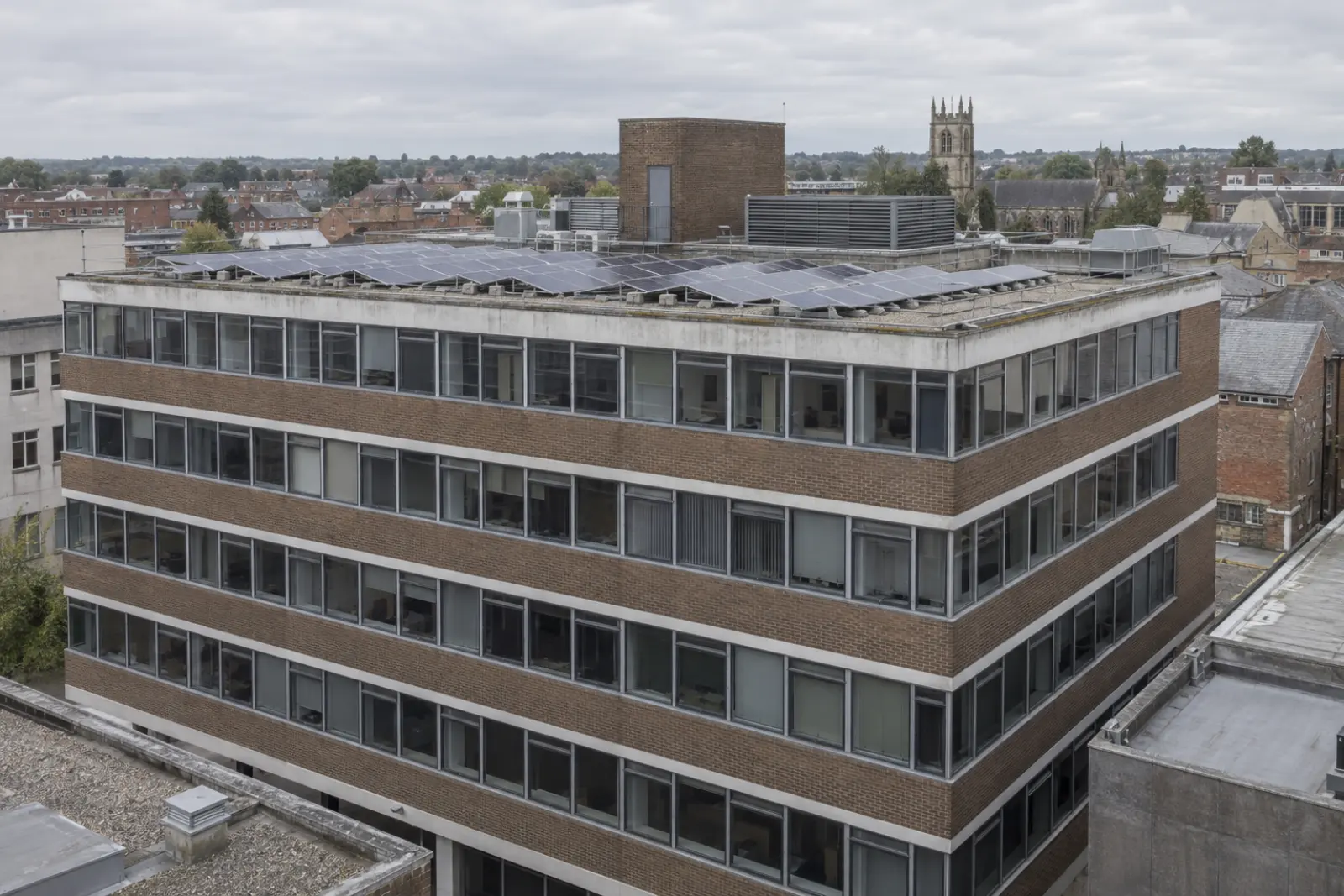 A town centre office block whose flat roof carries a lift overrun, a plant screen and a solar array on low frames