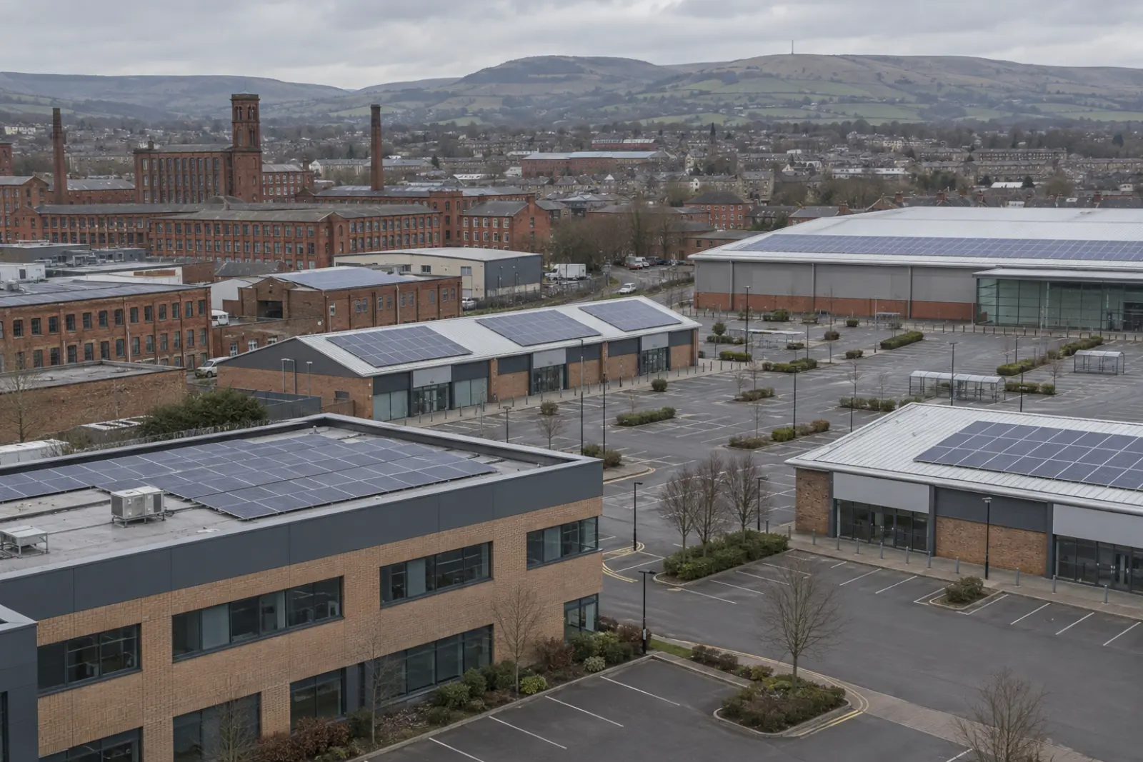 The commercial edge of a North West town, offices and a retail park with solar on several roofs, Pennine hills beyond