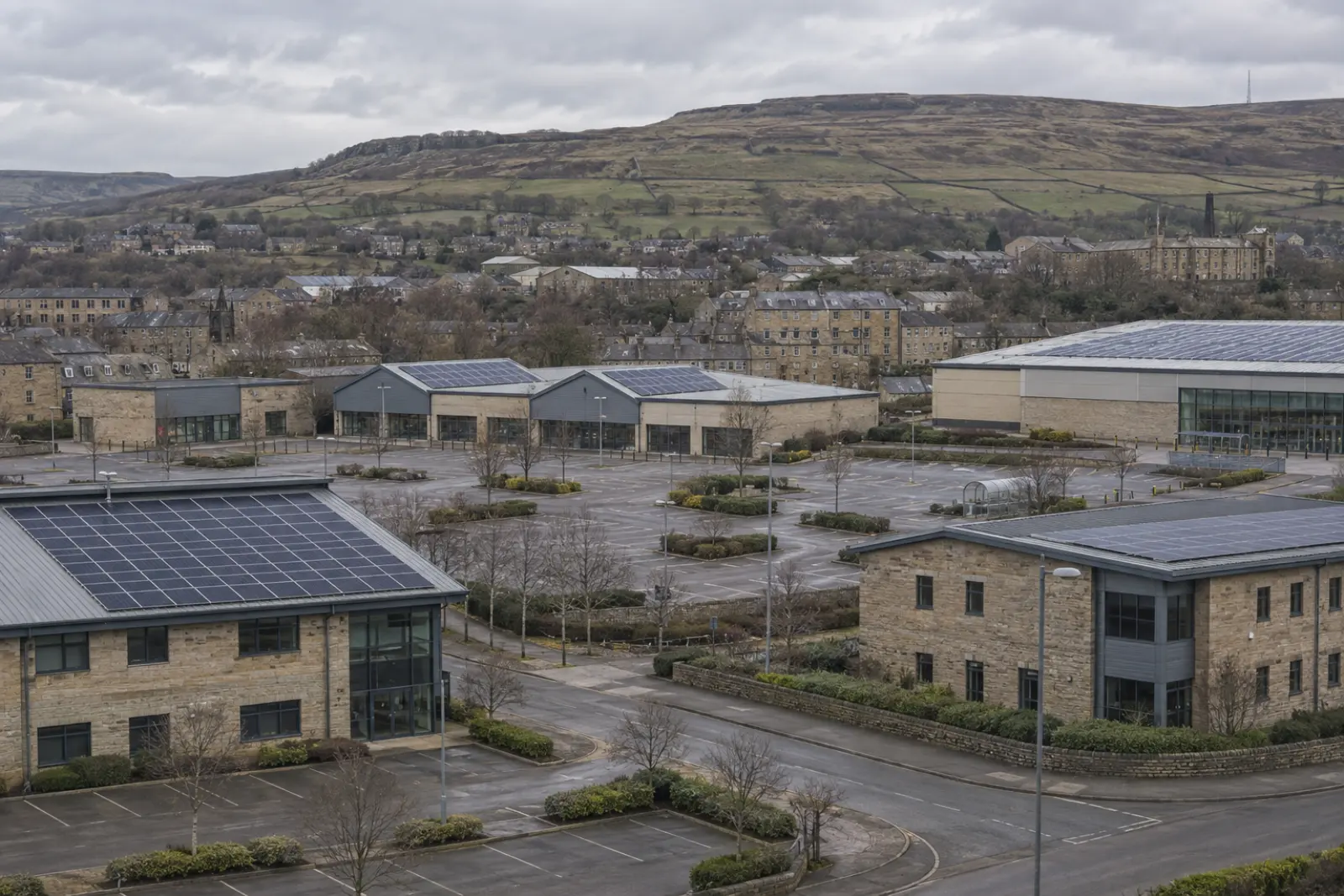 The commercial edge of a West Yorkshire town, several flat roofs carrying solar, moorland behind